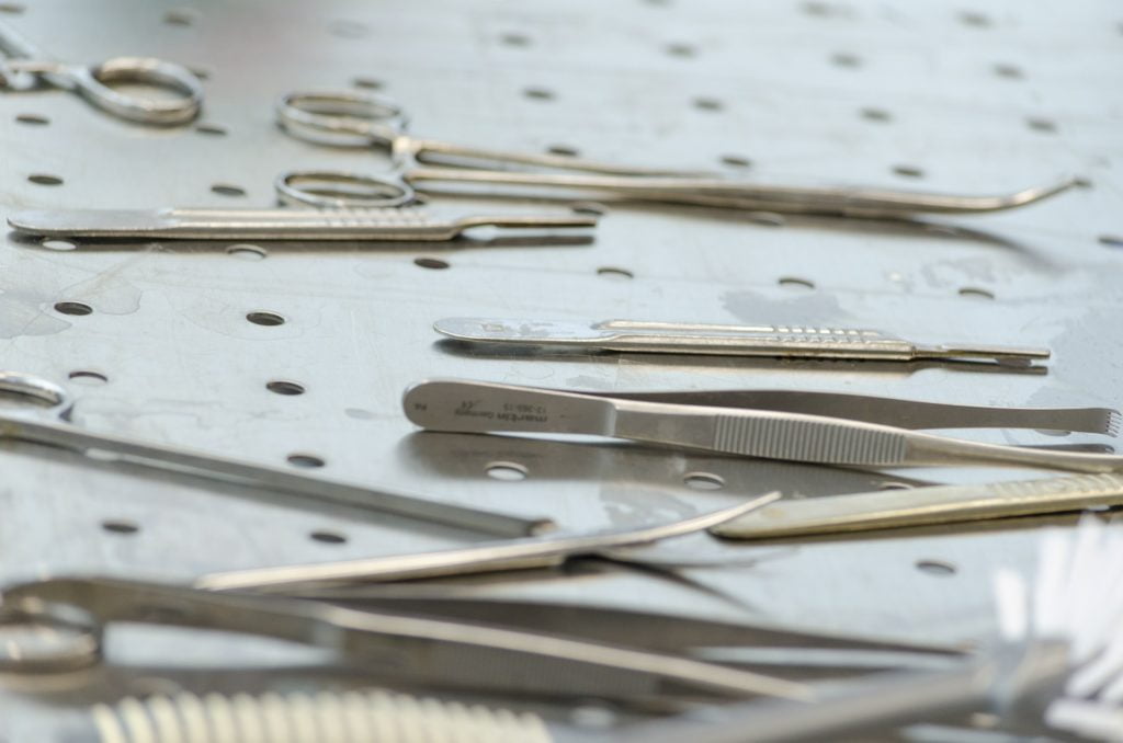 Metal surgical equipment (scalpels, forceps, probes etc) on a surgery tray with rows of holes in it