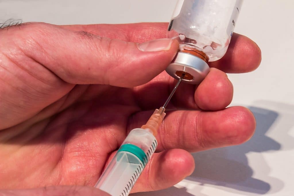 Photo of a white person's hands, shown filling a syringe from an ampoule/vial