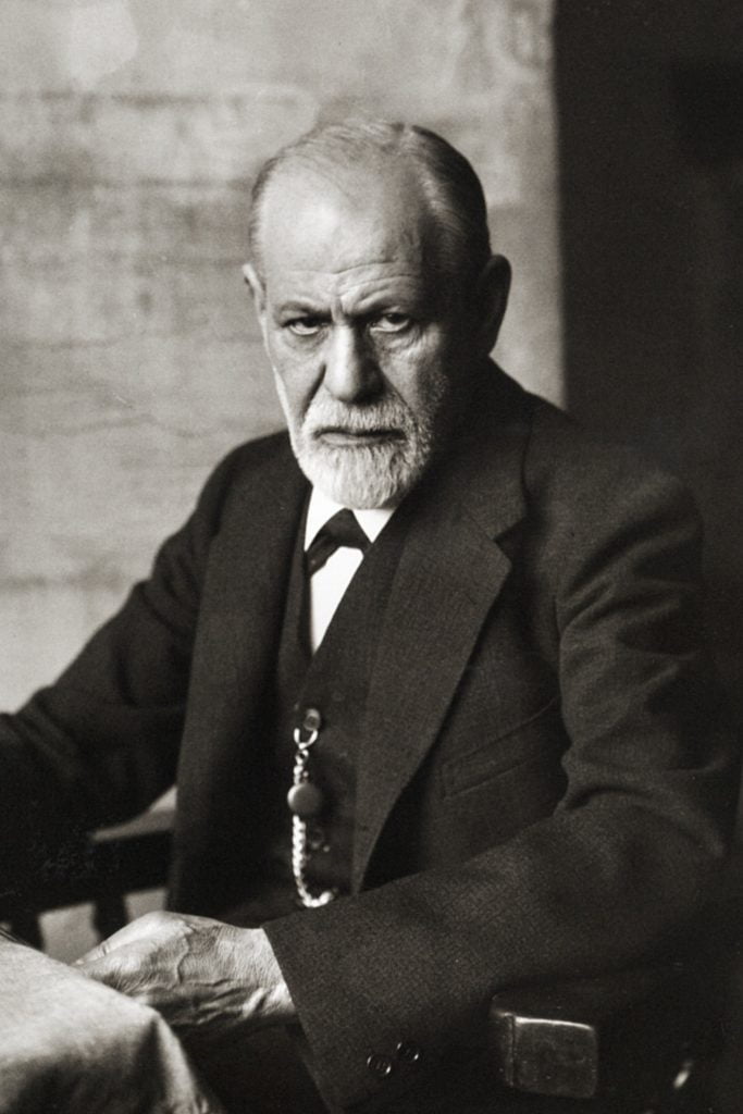 A photograph of Sigmund Freud - an older, white, straight-sized man with a white beard and thinning hair. He's wearing a three piece suit and looking at the camera quite sternly