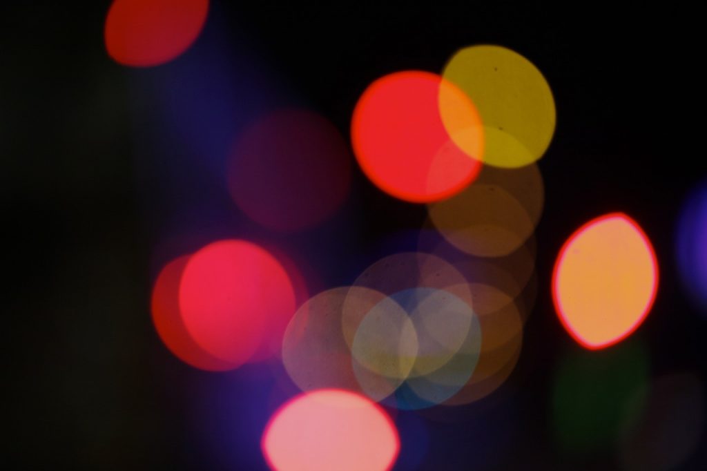 Fuzzy reflected/refracted circles of coloured lights; red, yellow, blue, pink and orange. Some are overlapping, on a dark background.