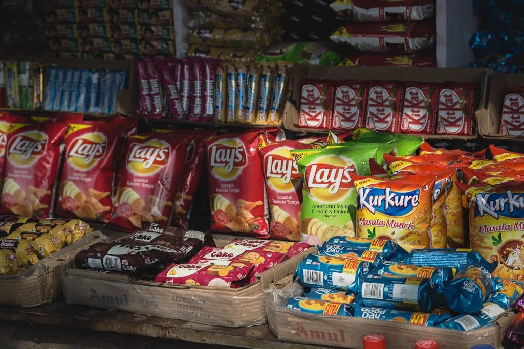 Chocolate bars, crisps, biscuits, cake and other snacks on an Indian food stand.