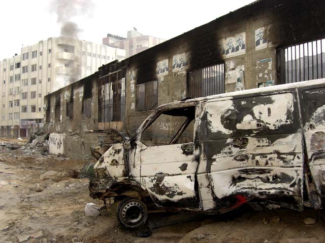 A destroyed white van stands in front of a burnt-out Al Quds hospital building after Israeli bombing in Gaza City.