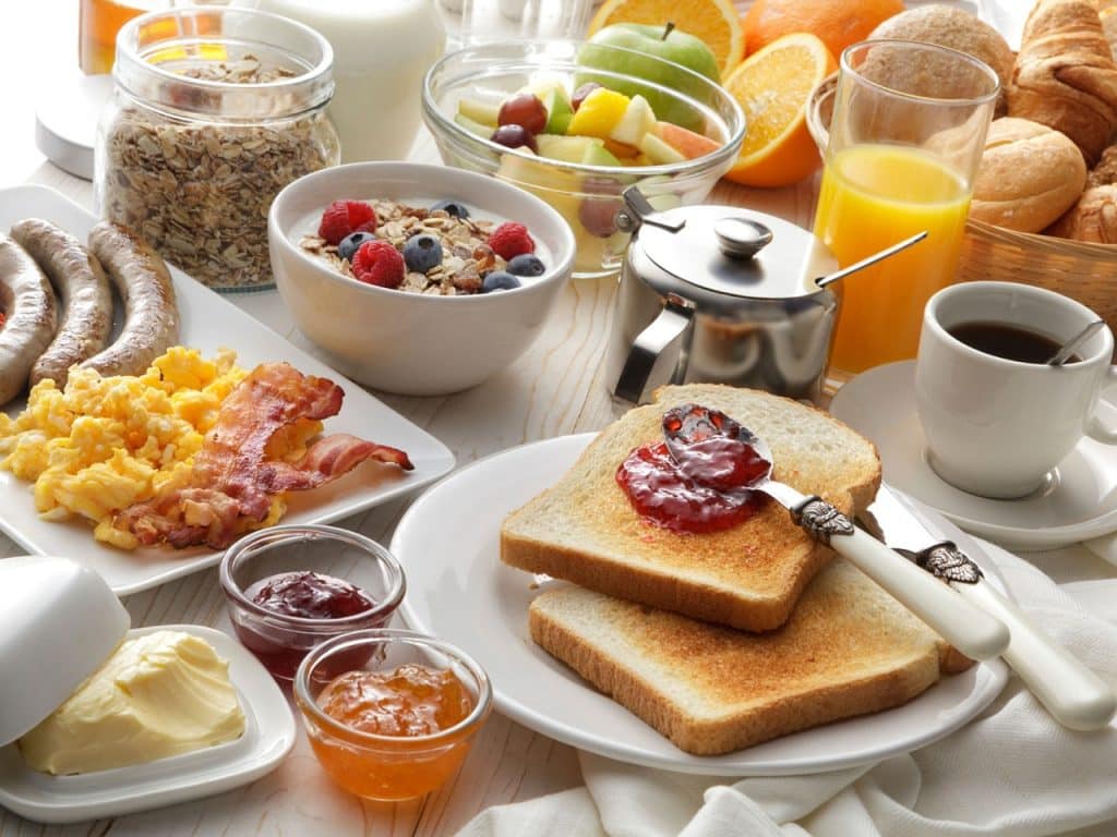 An array of breakfast foods and white crockery laid out in a large spread with coffee, spreads etc.