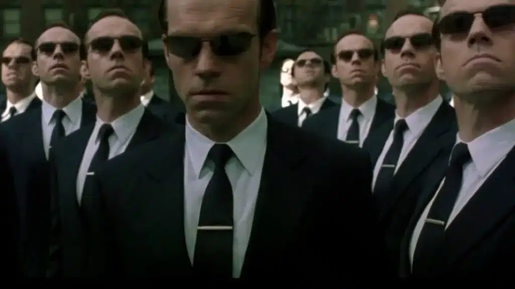 A flock of Agent Smiths (Hugo Weaving) in The Matrix Revolutions, dressed in their signature black suits and ties with silver tie clip and black sunglasses.