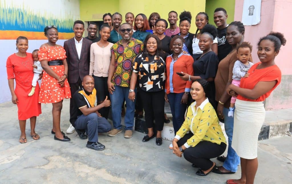 A large group of Lagos students, smiling, two in front kneeling, and two to either side each holding a baby