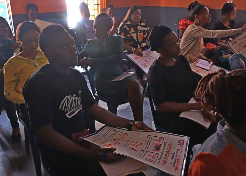 Lagos students in their classroom, thinking and discussing, holding large posters titled 'Critical reasoning'