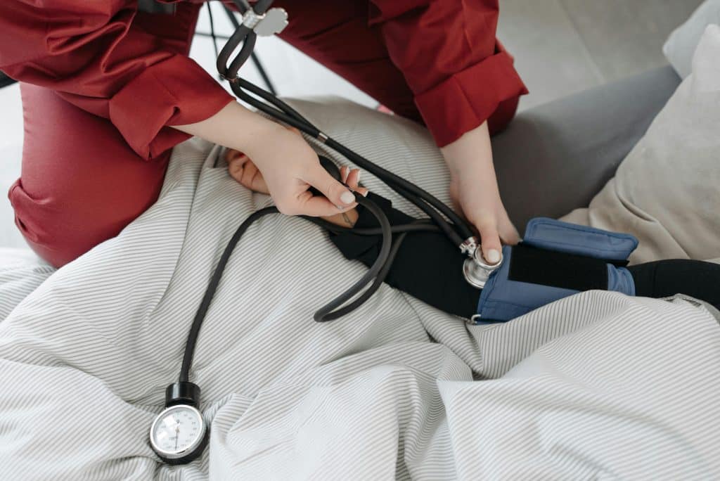 A paramedic in red checks a patient's blood pressure using a cuff and meter attached to their arm (a sphygmomanometer)