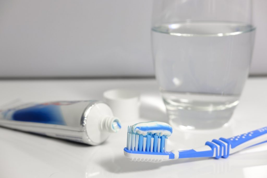 A blue and white toothbrush with blue and white toothpaste sitting atop its bristles, next to a tube of toothpaste and in front of a glass of water.