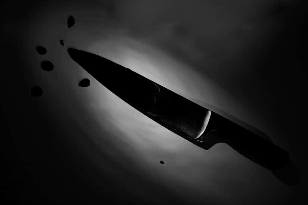 A low-light/monochrome photo of a kitchen knife on a surface, with suspect drips near its point