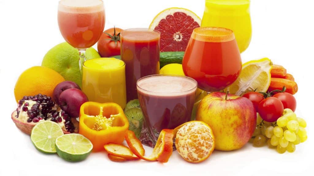 An artfully arranged array of citrus fruits and vegetables high in vitamin C, like apples, peppers, tomatoes and grapes. Six glasses of colourful juices also feature.